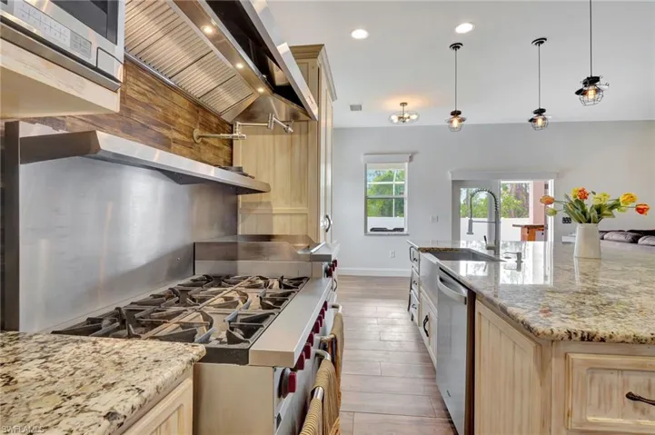Kitchen featuring custom cabinetry, light stone counters, stainless steel appliances and pendant lighting