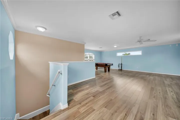 Below grade area featuring ornamental molding, light wood finished floors, healthy amount of natural light, billiards table, and ceiling fan