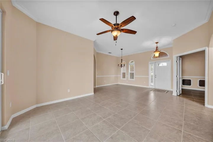 Unfurnished living room with ornamental molding, light tile patterned flooring, ceiling fan, and a chandelier
