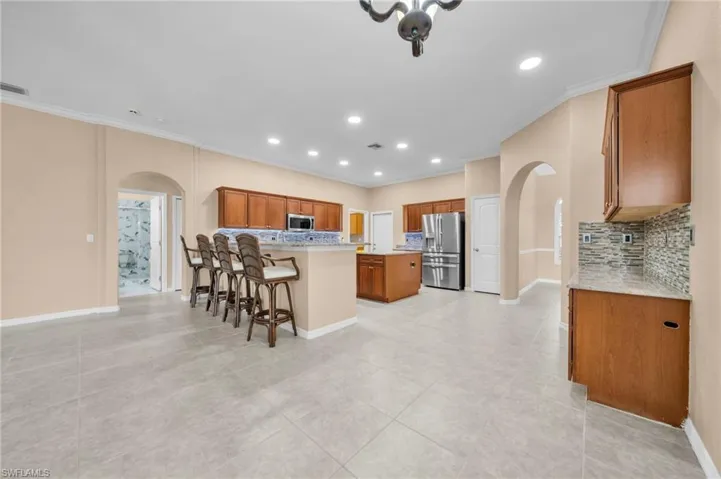 Kitchen featuring arched walkways, a kitchen breakfast bar, brown cabinets, ornamental molding, and appliances with stainless steel finishes