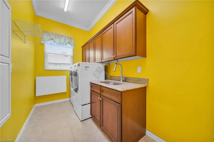 Laundry room featuring ornamental molding, cabinet space, light tile patterned flooring, and washer and dryer