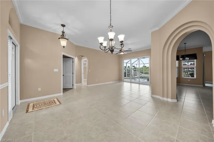 Unfurnished dining area featuring arched walkways, a chandelier, ornamental molding, light tile patterned floors, and ceiling fan