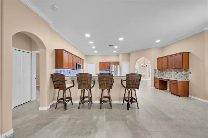 Kitchen with arched walkways, decorative backsplash, a breakfast bar area, ornamental molding, and recessed lighting