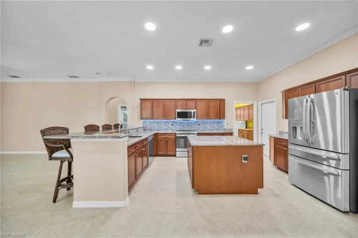 Kitchen with brown cabinets, stainless steel appliances, a breakfast bar, ornamental molding, and backsplash