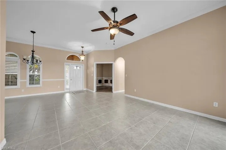 Unfurnished living room featuring light tile patterned floors, ornamental molding, arched walkways, a chandelier, and ceiling fan