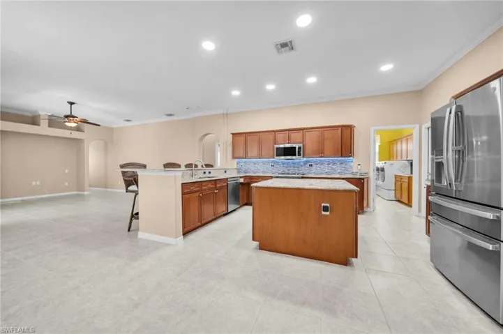 Kitchen featuring crown molding, arched walkways, a breakfast bar, brown cabinets, and appliances with stainless steel finishes