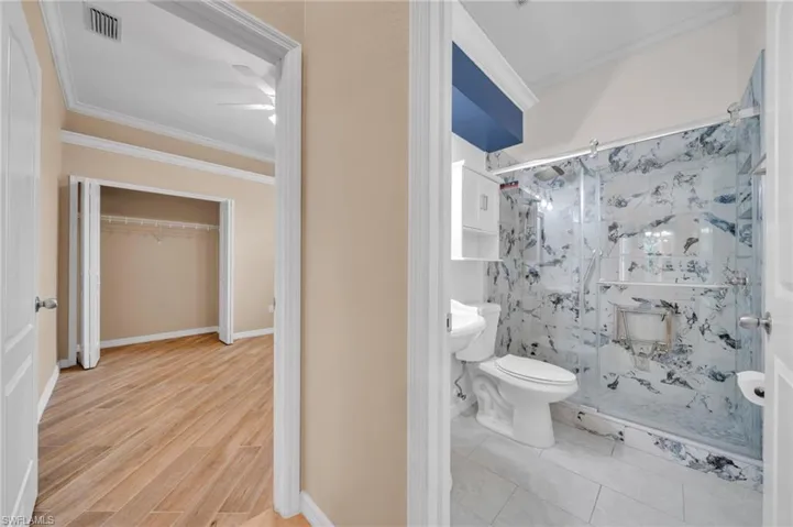 Bathroom with ornamental molding, a shower stall, and light wood-style flooring