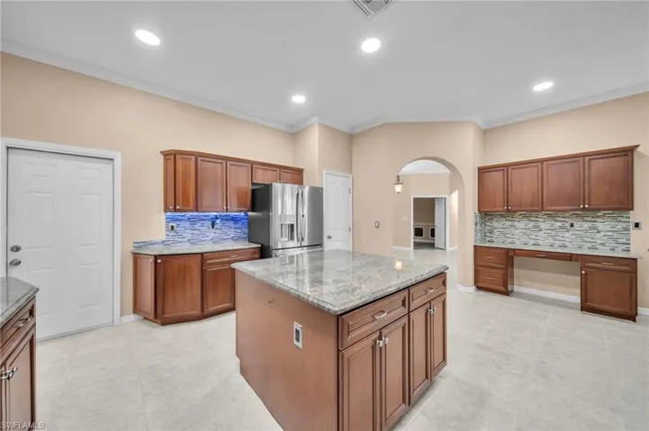 Kitchen featuring tasteful backsplash, arched walkways, crown molding, brown cabinetry, and stainless steel fridge with ice dispenser