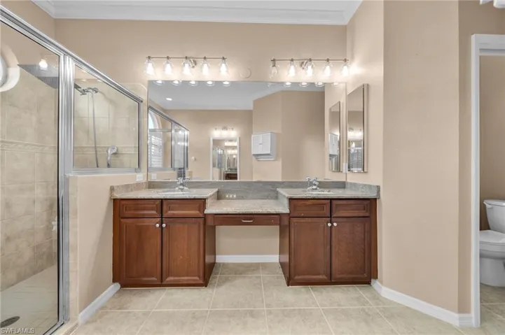 Full bath with a stall shower, double vanity, light tile patterned floors, and ornamental molding