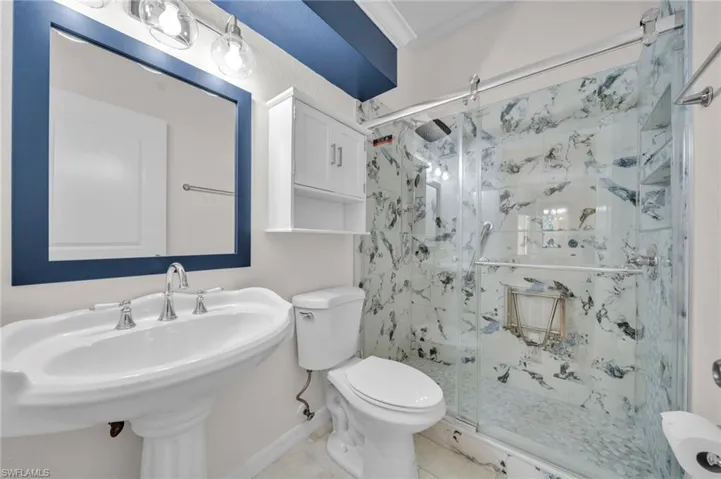 Full bath featuring a marble finish shower, ornamental molding, and tile patterned flooring