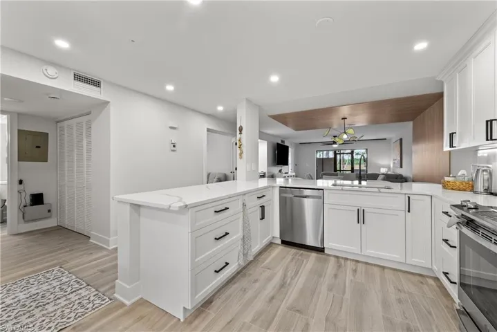 Kitchen with open floor plan, white cabinetry, light stone countertops, a peninsula, and stainless steel appliances