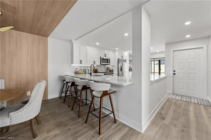 Kitchen featuring a breakfast bar, a peninsula, wood finish floors, white cabinets, and light stone countertops