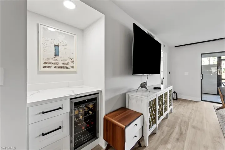 Bar area featuring beverage cooler, light stone countertops, white cabinetry, and light wood-type flooring