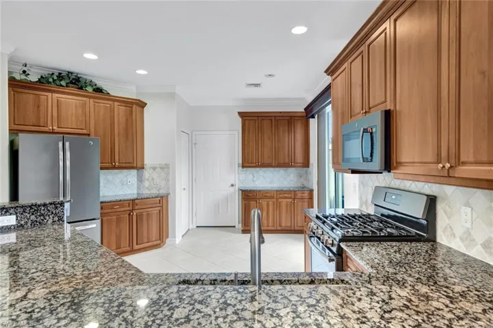 Kitchen with stainless steel appliances, wood finish cabinetry, crown molding, light tile patterned flooring, and dark stone countertops