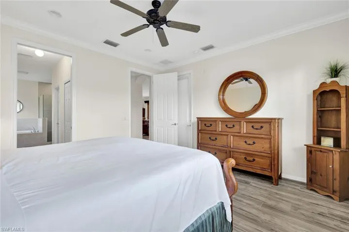 Bedroom featuring ornamental molding, light wood-style floors, a ceiling fan, and ensuite bath