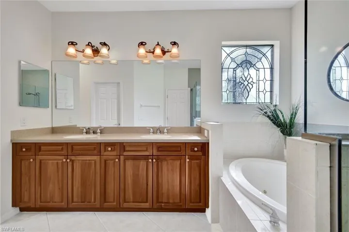 Full bathroom with double vanity, a jetted tub, and light tile patterned floors