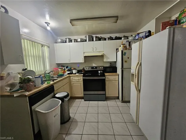 Kitchen featuring white fridge with ice dispenser, stainless steel range with electric stovetop, freestanding refrigerator, black microwave, and under cabinet range hood