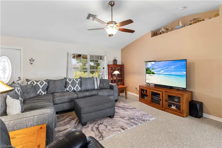 Living room with vaulted ceiling, carpet flooring, and a ceiling fan