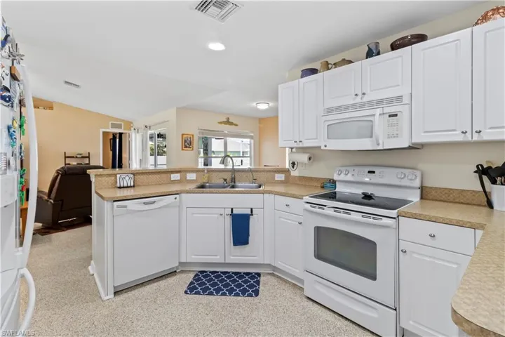 Kitchen with white appliances, a peninsula, light countertops, white cabinetry, and recessed lighting