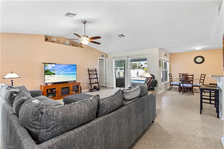 Living area with ceiling fan, vaulted ceiling, and dark aggregate flooring