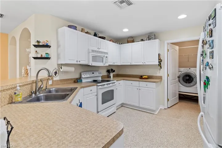 Kitchen with white appliances, white cabinetry, washer / clothes dryer, recessed lighting, and light countertops