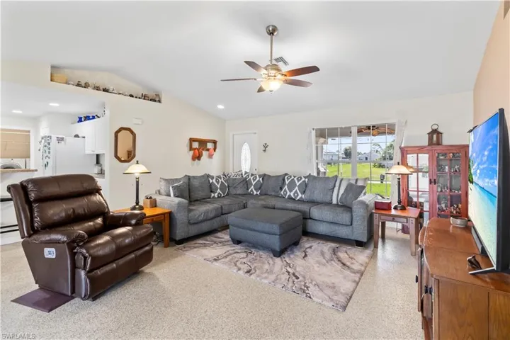 Living room with vaulted ceiling, ceiling fan, and dark aggregate flooring