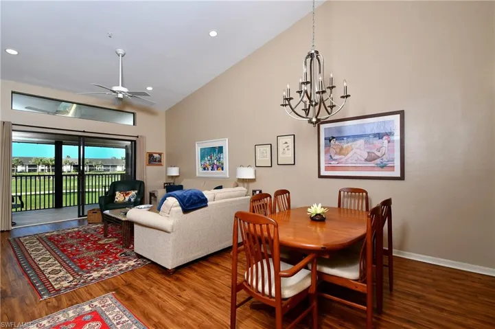 Dining area with ceiling fan with notable chandelier, hardwood / wood-style flooring, and high vaulted ceiling