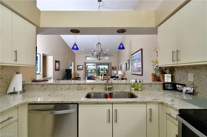 Kitchen with backsplash, sink, stainless steel dishwasher, a notable chandelier, and light stone counters