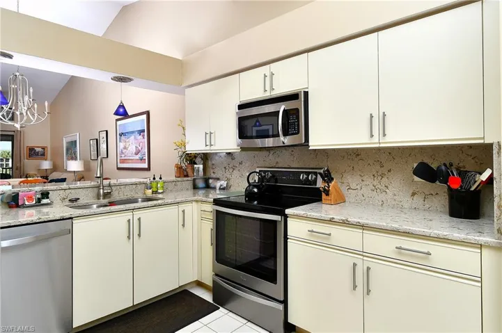 Kitchen featuring sink, stainless steel appliances, tasteful backsplash, vaulted ceiling, and light tile patterned flooring