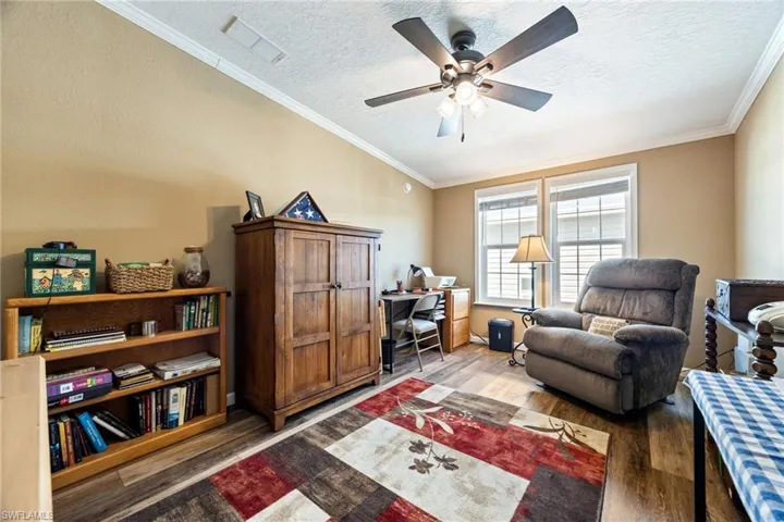 Sitting room with an office area, wood finished floors, a textured ceiling, crown molding, and a ceiling fan