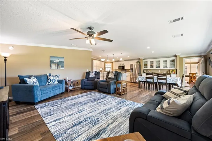 Living area featuring crown molding, dark wood-style floors, and ceiling fan