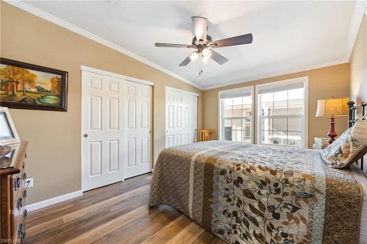 Bedroom with two closets, ornamental molding, wood finished floors, vaulted ceiling, and a ceiling fan