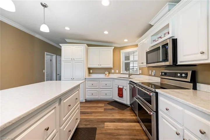 Kitchen with stainless steel appliances, white cabinetry, decorative light fixtures, crown molding, and dark wood-type flooring