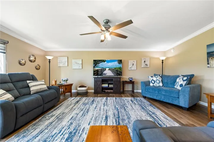 Living room with wood finished floors, ceiling fan, and crown molding