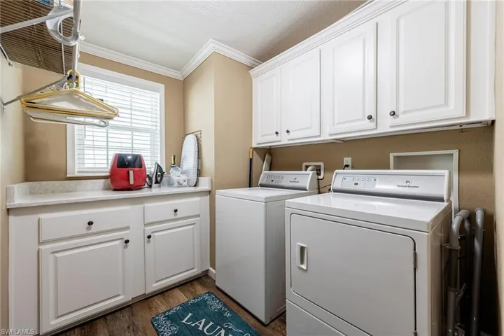 Laundry room with crown molding, cabinet space, dark wood-type flooring, washer and clothes dryer, and a textured ceiling