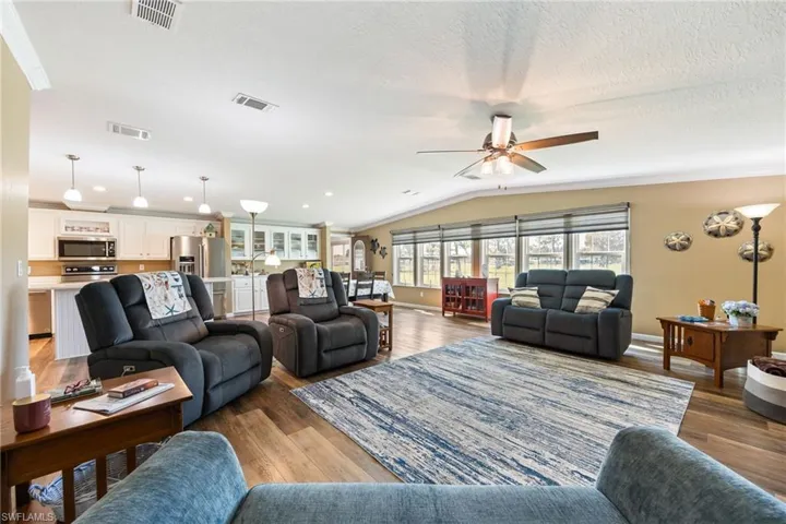 Living room with wood finished floors, lofted ceiling, a ceiling fan, and ornamental molding