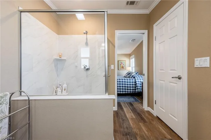 Ensuite bathroom featuring a marble finish shower, crown molding, and dark wood-style flooring