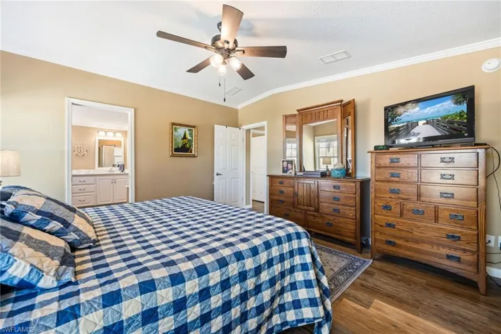 Bedroom featuring crown molding, a ceiling fan, dark wood-style floors, and connected bathroom