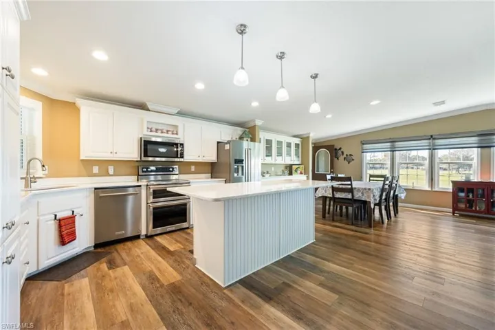 Kitchen with white cabinetry, stainless steel appliances, hanging light fixtures, a center island, and dark wood-style floors