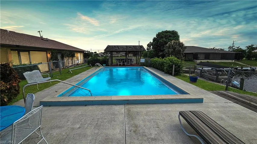 Pool at dusk with a lawn, a patio area, and a pergola