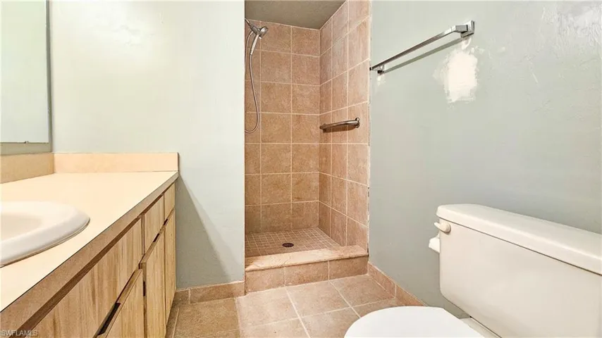 Bathroom featuring tiled shower, vanity, toilet, and tile patterned flooring