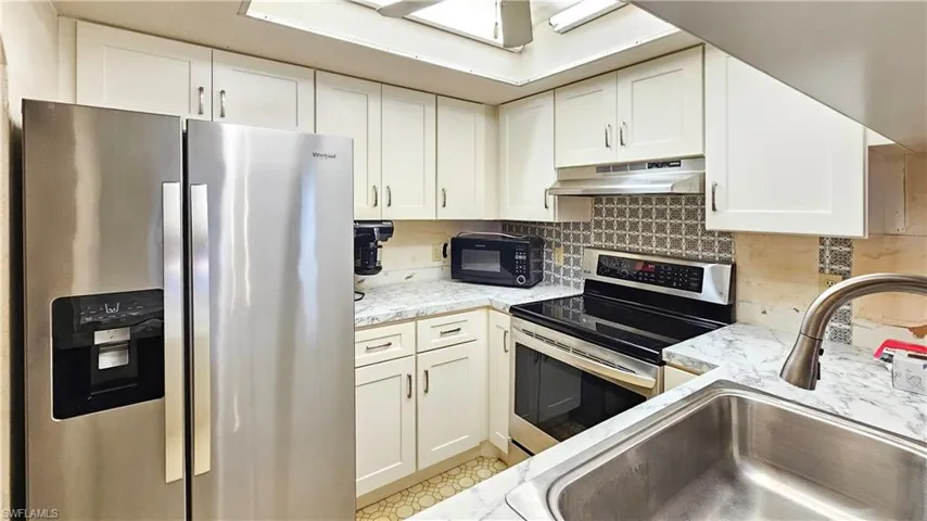 Kitchen featuring ventilation hood, white cabinets, stainless steel appliances, sink, and tasteful backsplash