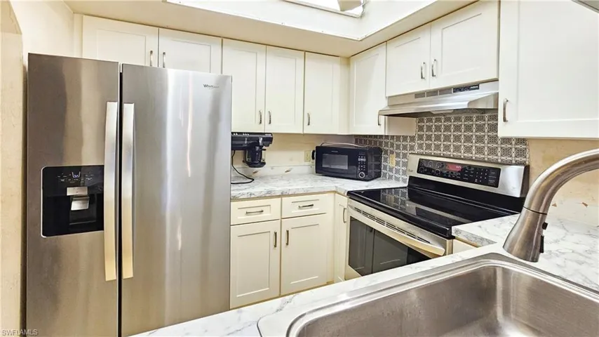 Kitchen with white cabinets, backsplash, light stone counters, stainless steel appliances, and sink