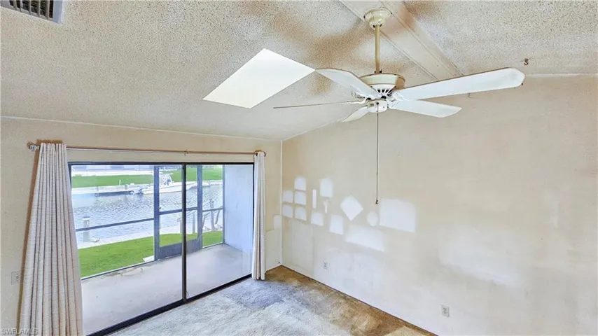 Carpeted empty room featuring a textured ceiling, lofted ceiling with skylight, and ceiling fan