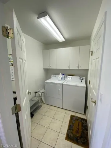 Laundry area featuring light tile patterned flooring, washing machine and clothes dryer, and cabinet space