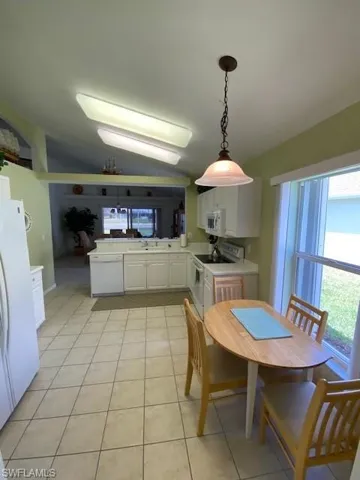 Kitchen with lofted ceiling, white cabinetry, white appliances, light countertops, and hanging light fixtures