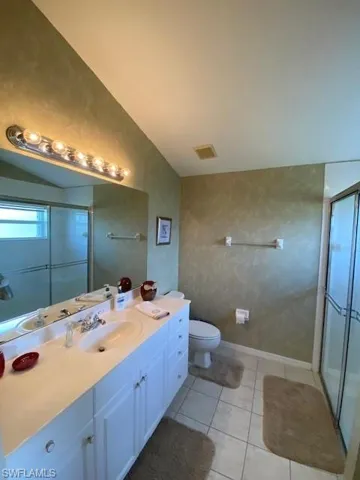 Bathroom with a shower stall, vanity, light tile patterned floors, and vaulted ceiling