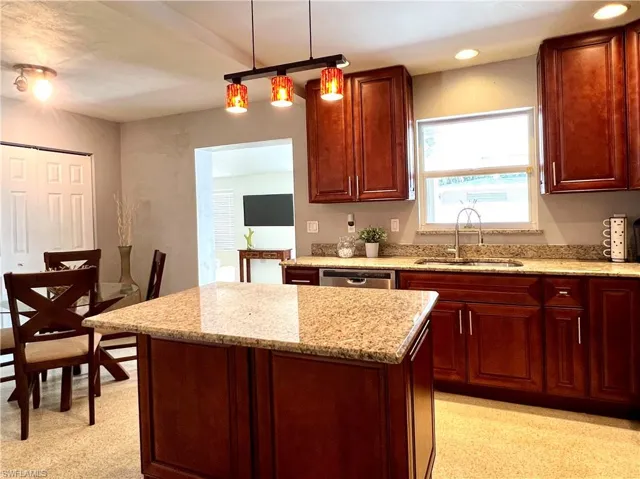 Kitchen featuring a sink, a kitchen island, light stone countertops, pendant lighting, and dishwasher