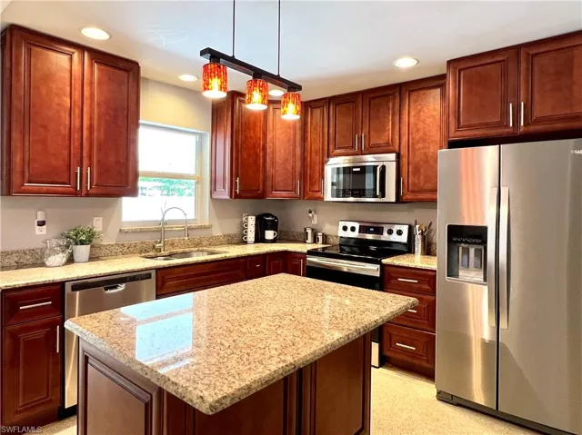 Kitchen featuring stainless steel appliances, a sink, recessed lighting, light stone counters, and decorative light fixtures