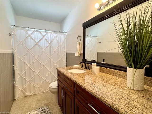 Hall Bathroom featuring tile walls, wainscoting, toilet, vanity, and curtained shower